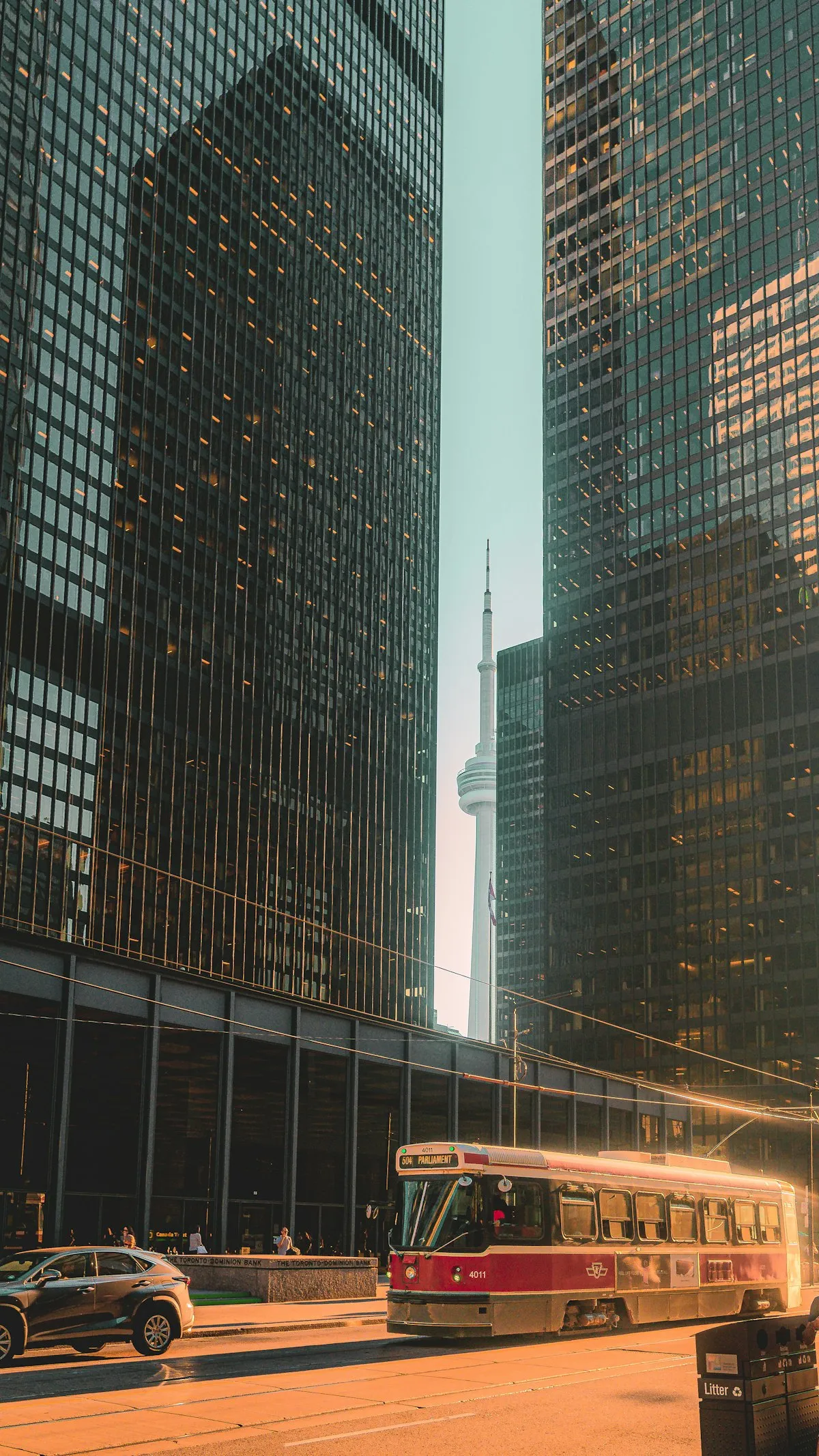 A Toronto streetcar rolls through downtown at golden hour with the CN Tower rising in the background