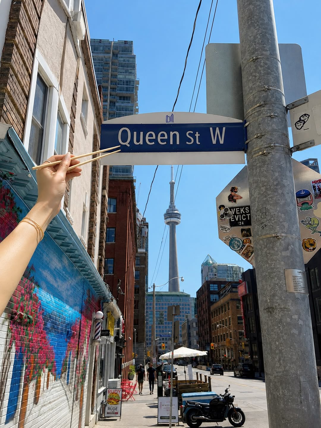 Chopsticks pointing at a Queen St W street sign with the CN Tower behind, posted by @kajikencanada — location teaser, not a Kajiken storefront