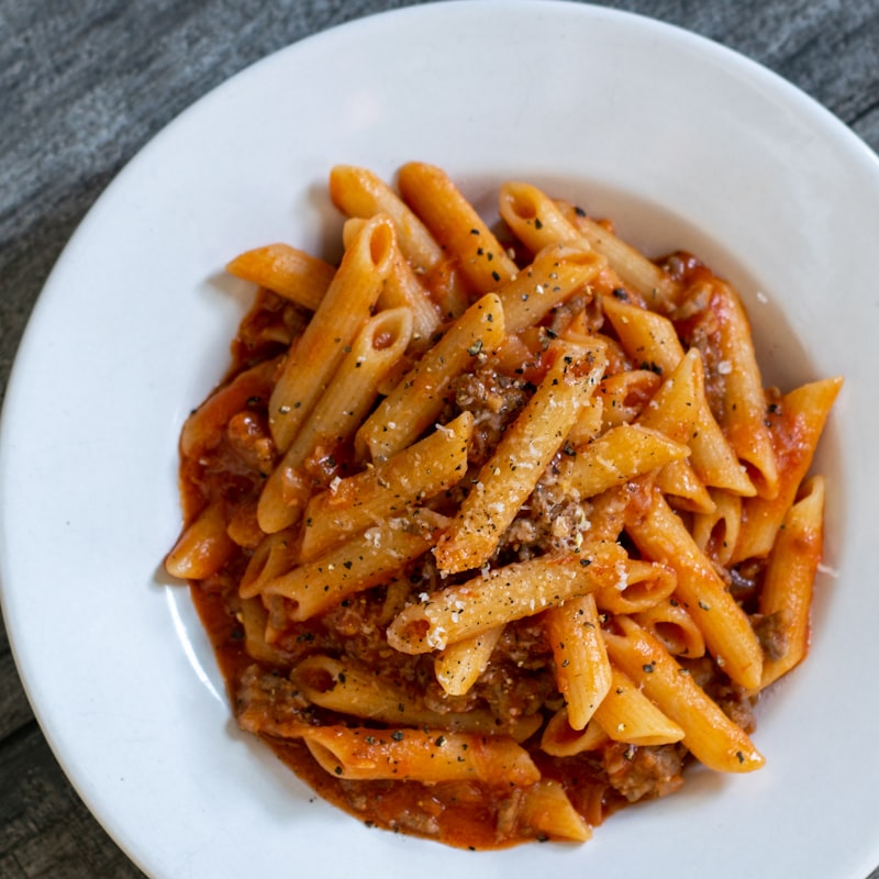 Artisanal fresh pasta with rich Italian sauce and fresh herbs on a white plate