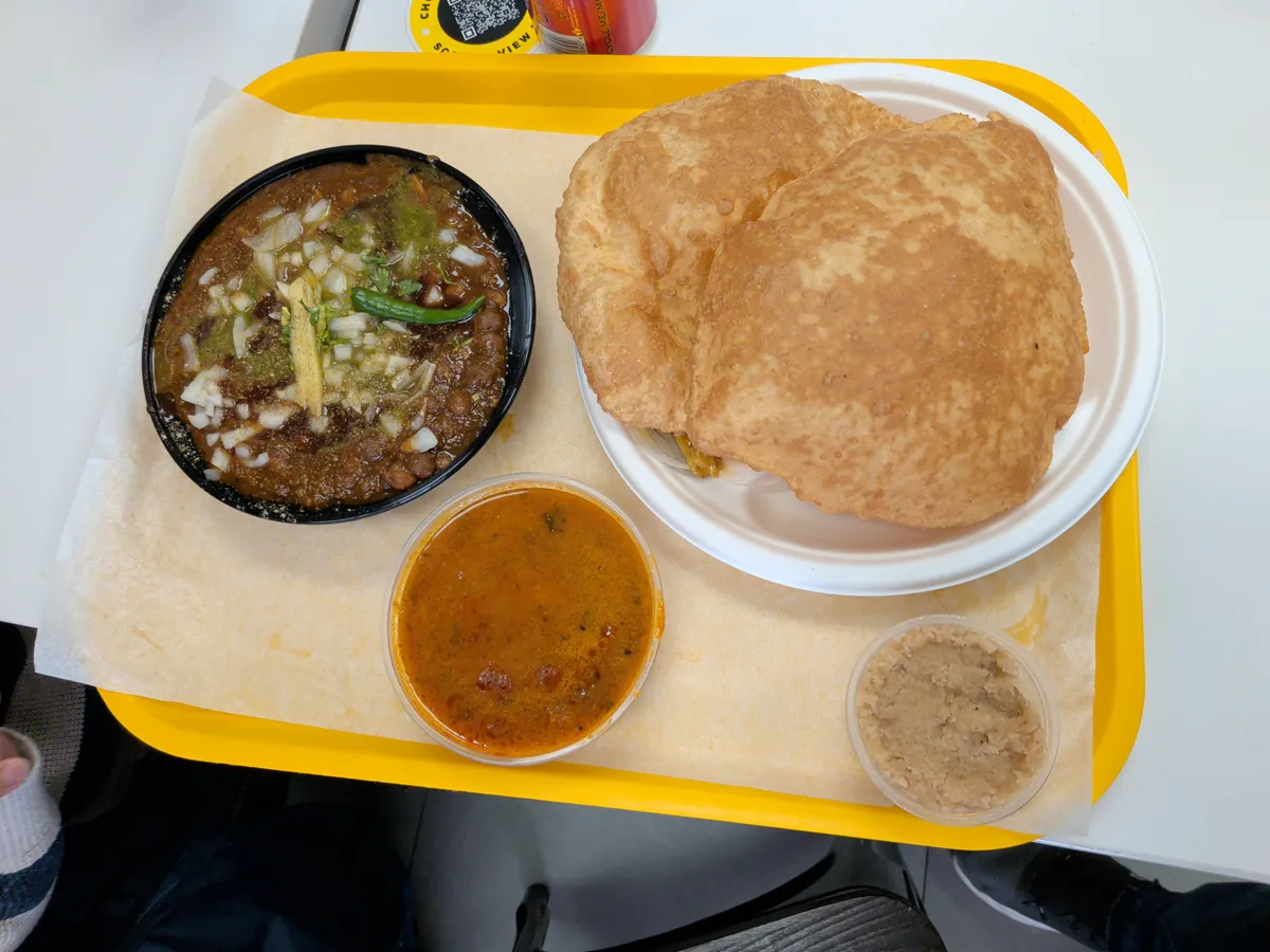 A tray featuring two golden bhaturas, a bowl of chole, and a side of halwa