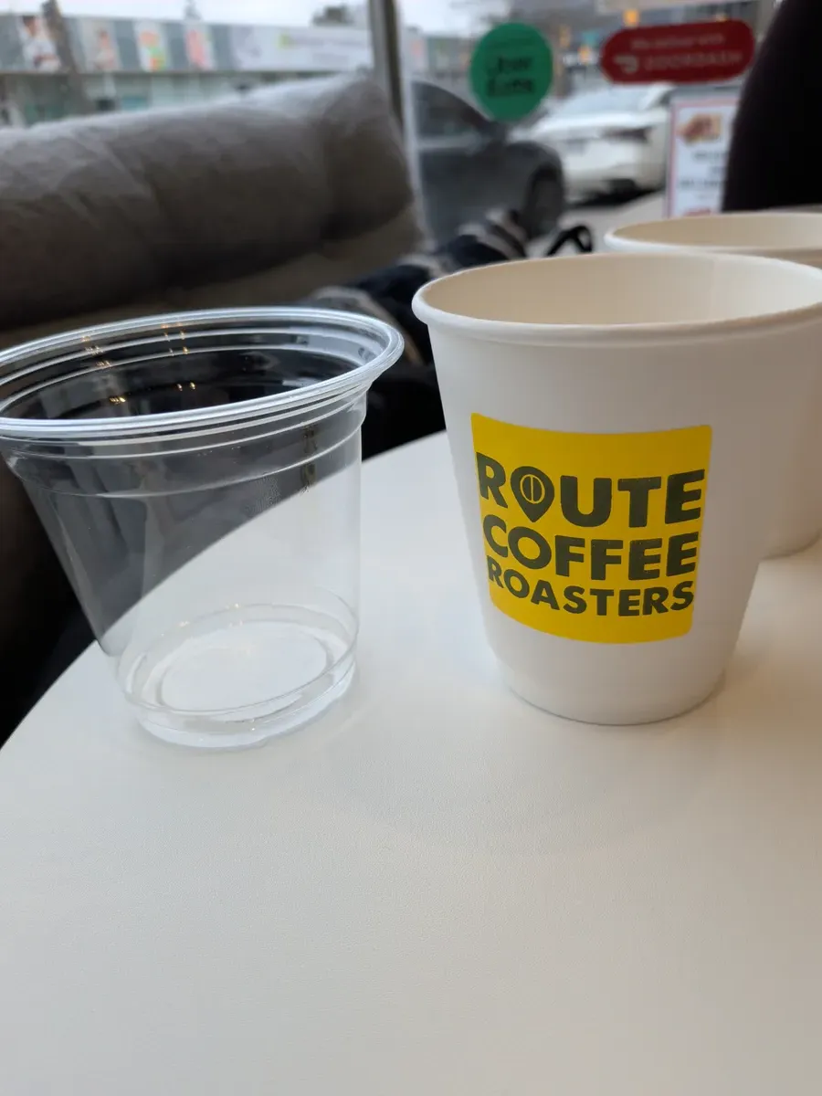 A branded Route Coffee Roasters paper cup next to an empty plastic cup