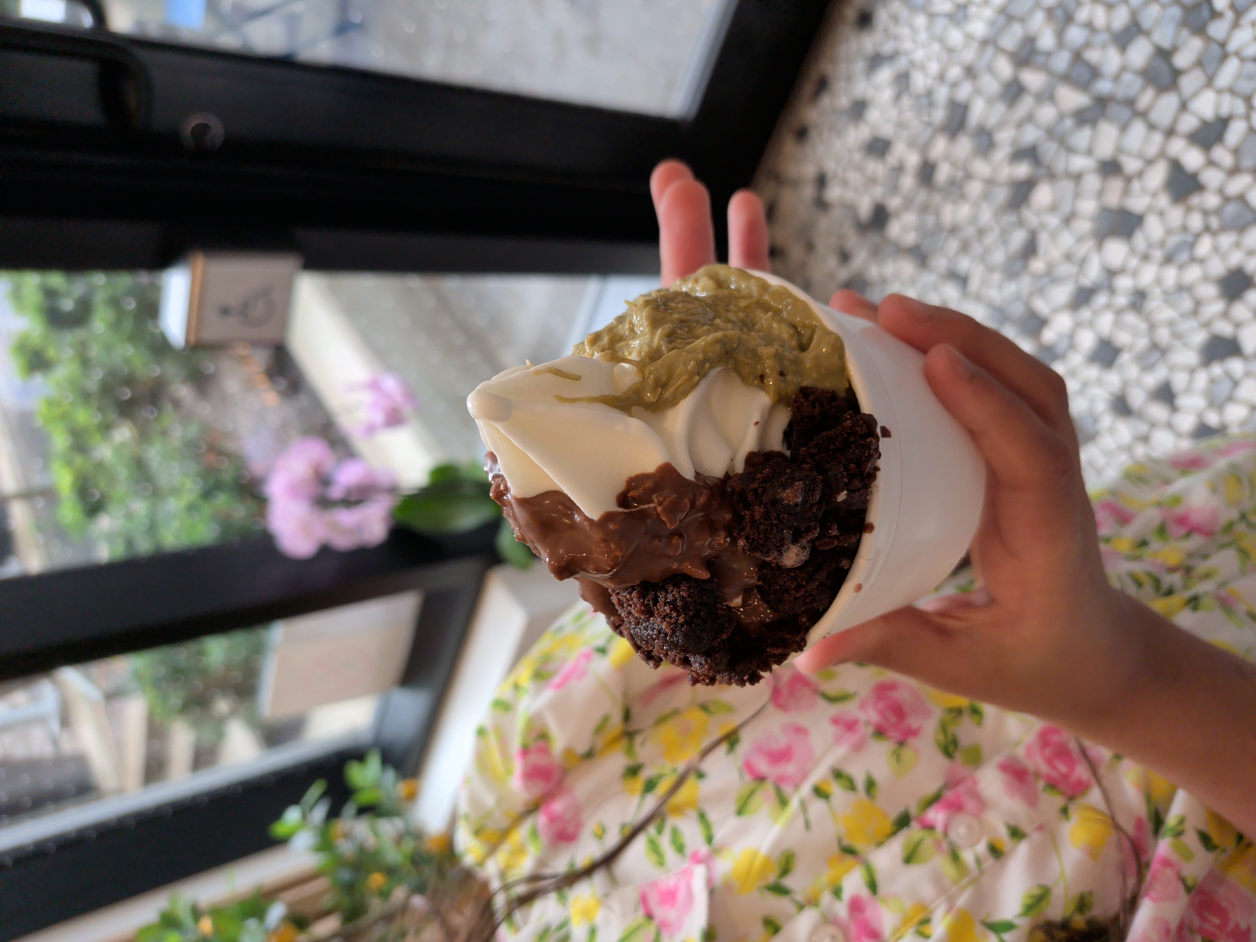 A cup of frozen yogurt swirled with chocolate and pistachio toppings