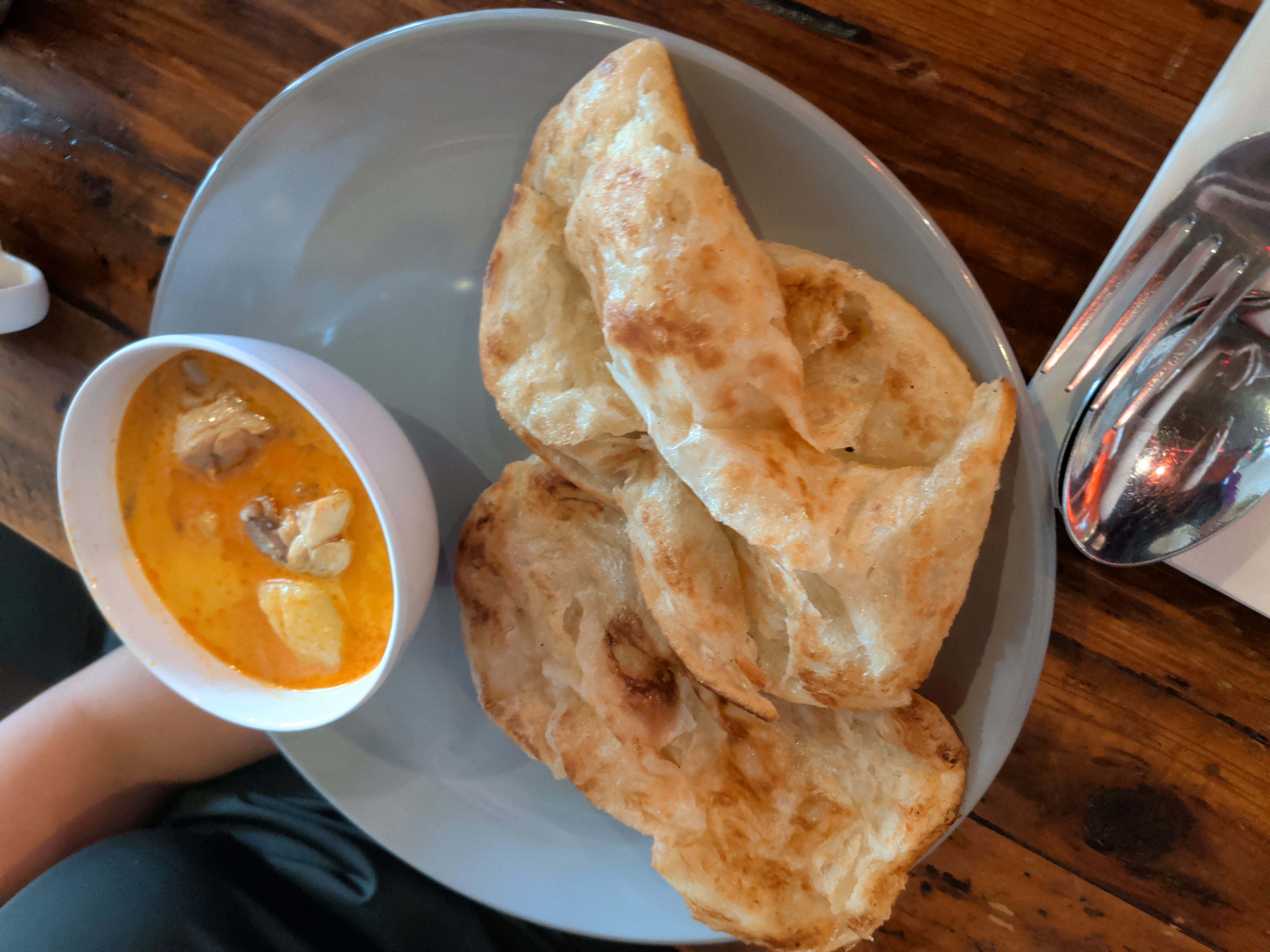 A grey plate holding crispy folded roti next to a small bowl of creamy yellow curry with chicken pieces.