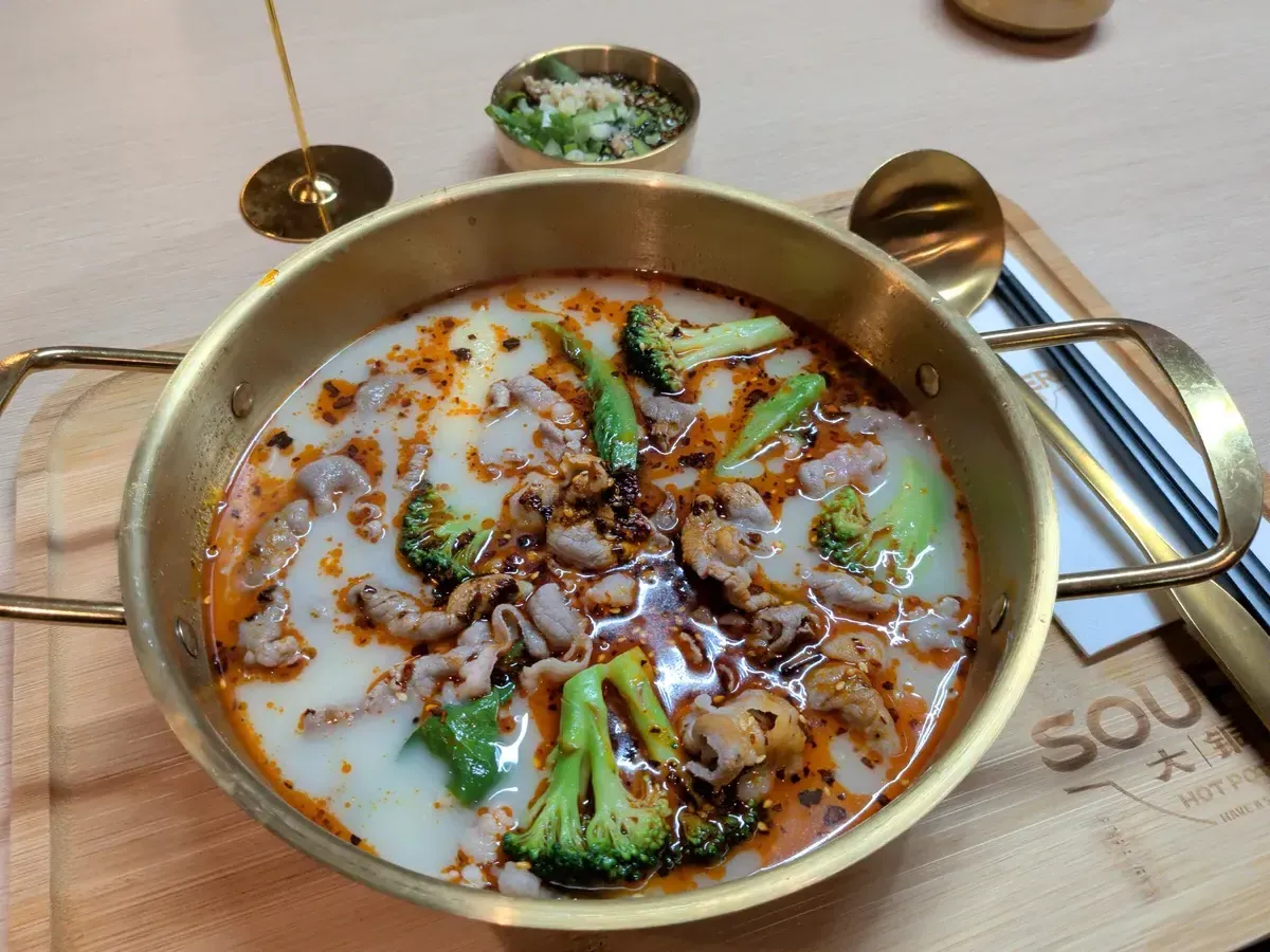 A golden hot pot bowl filled with broth, meat, and vegetables