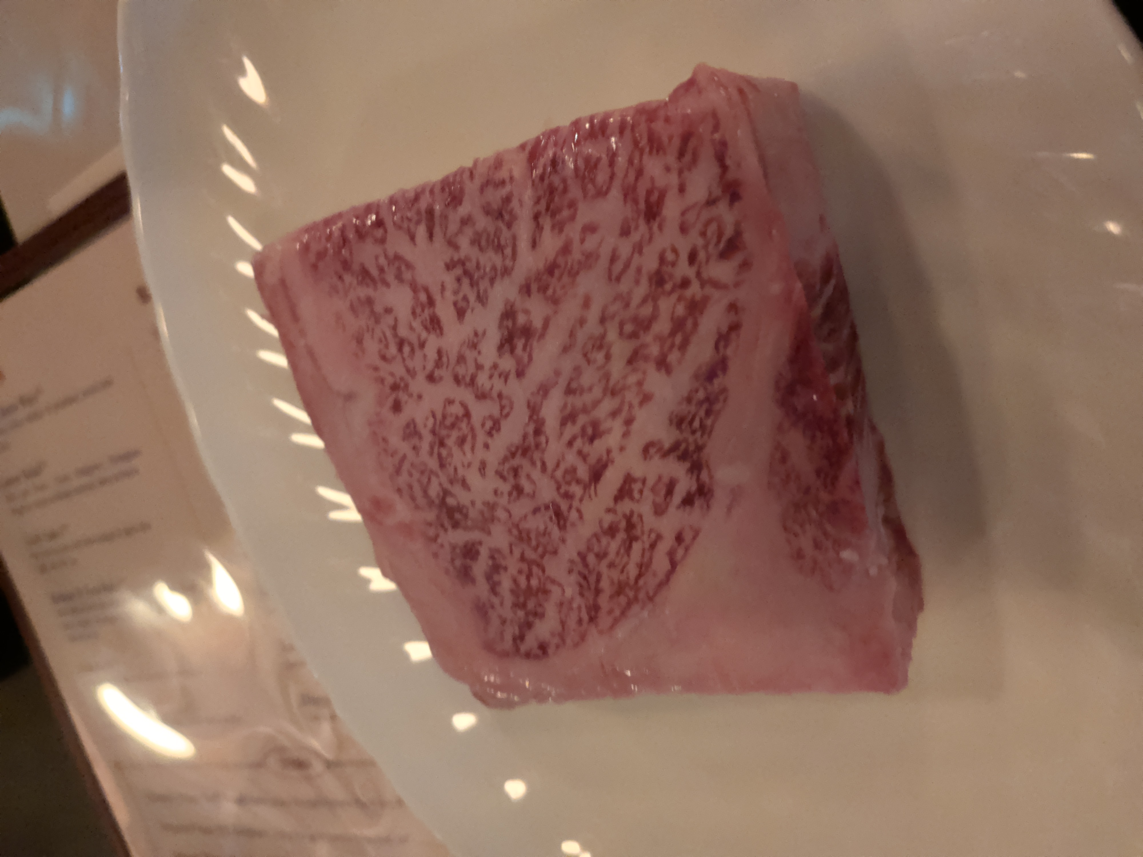 Raw six-ounce Japanese A5 wagyu striploin, heavily marbled, on a white plate
