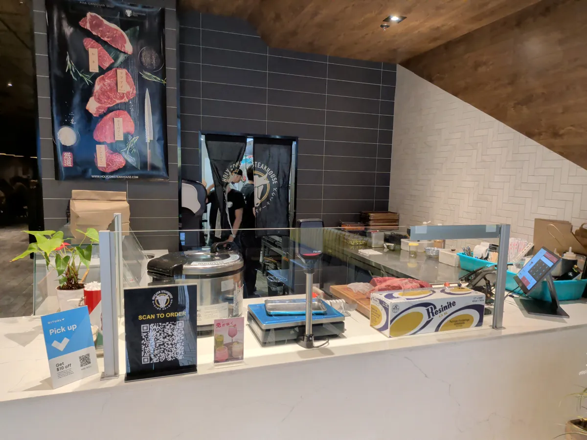 The service counter at Holy Cow Steakhouse with a QR code for ordering and a view into the kitchen.