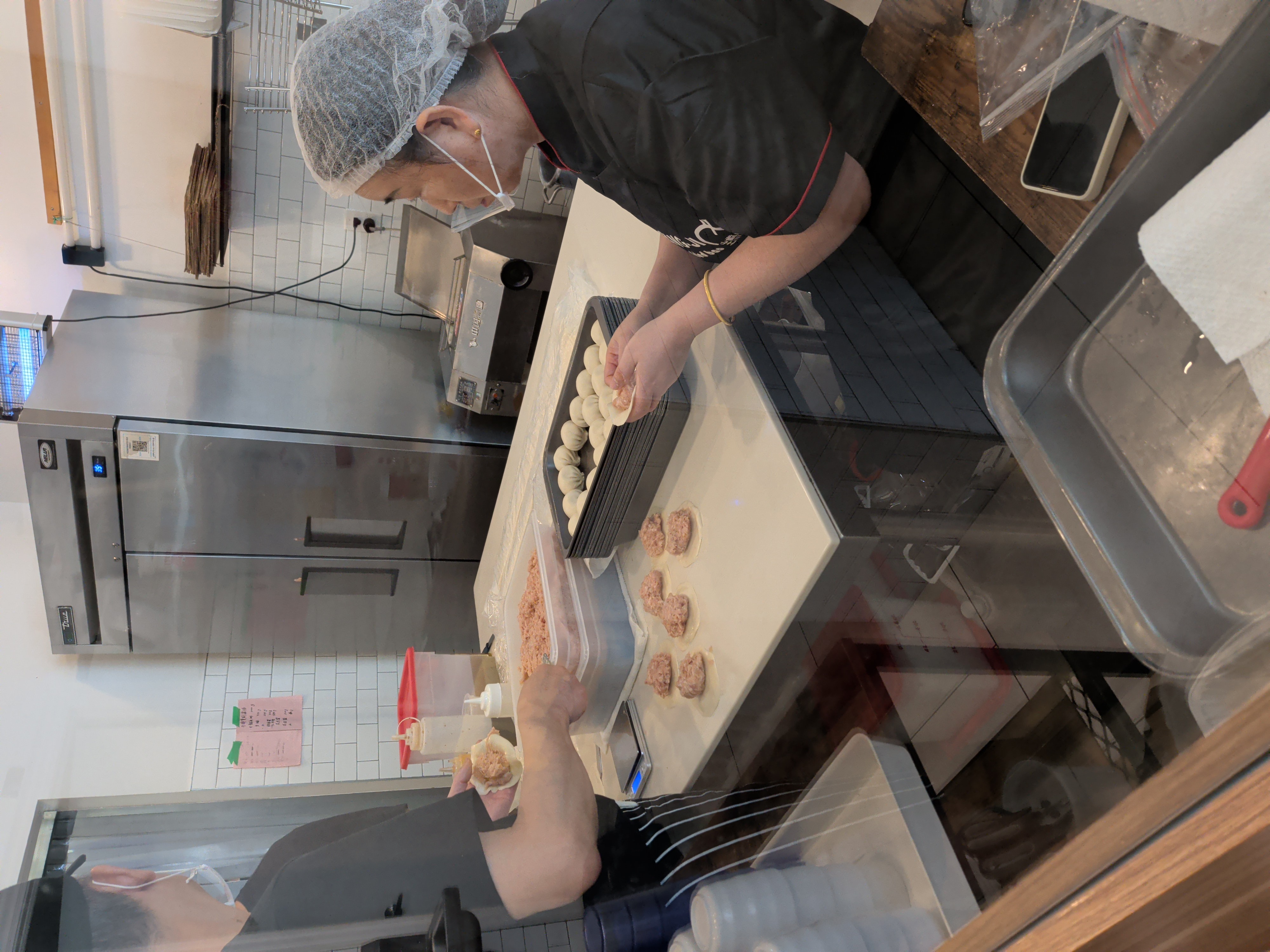 Cooks folding sheng jian bao behind the kitchen glass