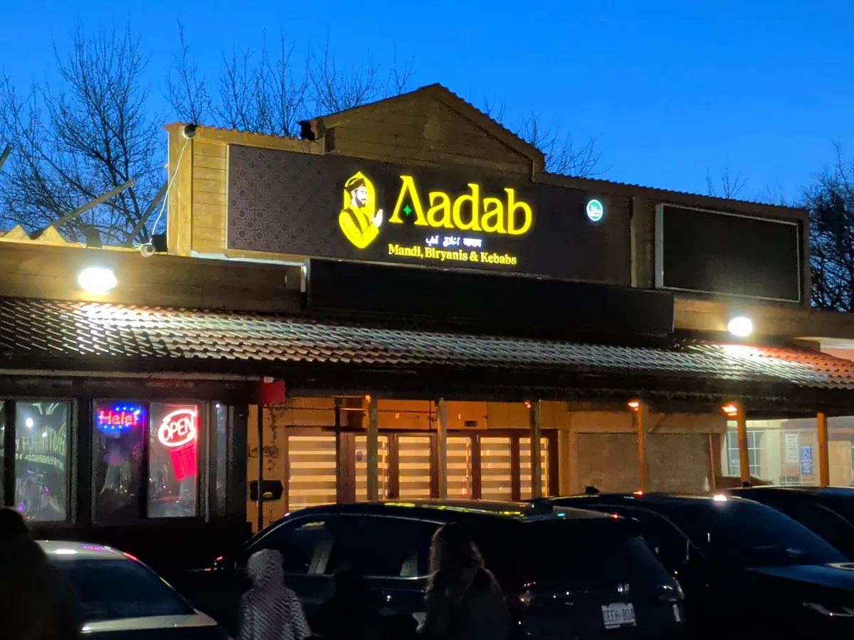 Nighttime storefront of Aadab on Kennedy Road in Scarborough, yellow Mandi Biryanis & Kebabs sign